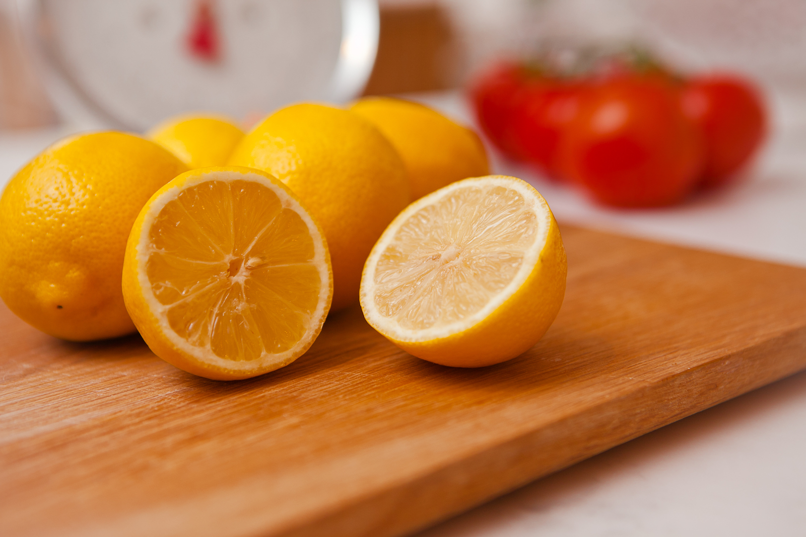 cut lemons displayed on a chopping board, tomatoes are out of focus in the background