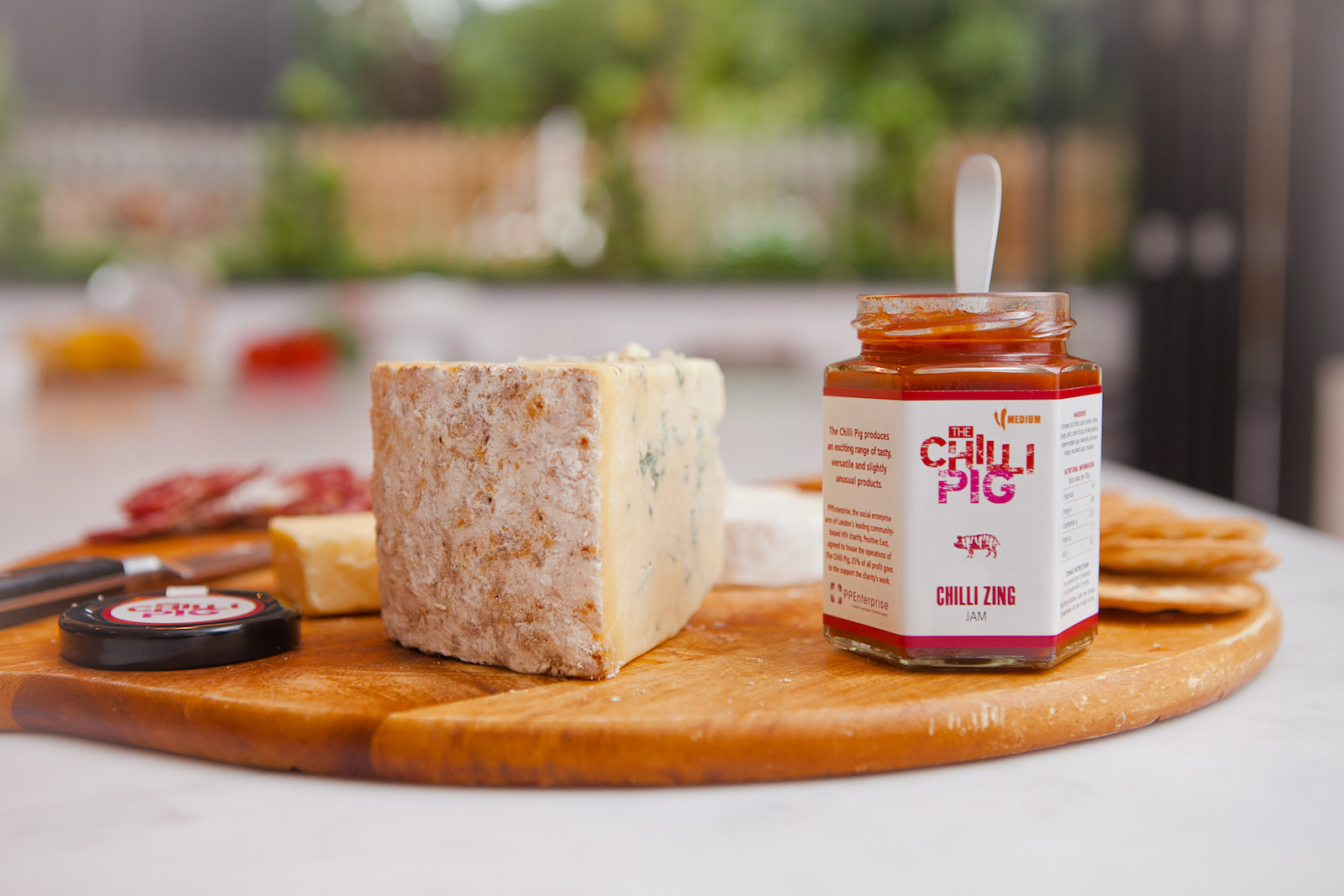 Open jar of chilli sauce next to some cheese on a cutting board